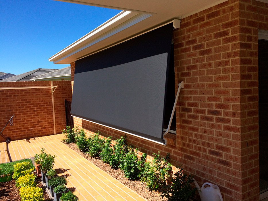 Backyard patio with brick wall, potted plants, and a large black retractable awning attached to the house.