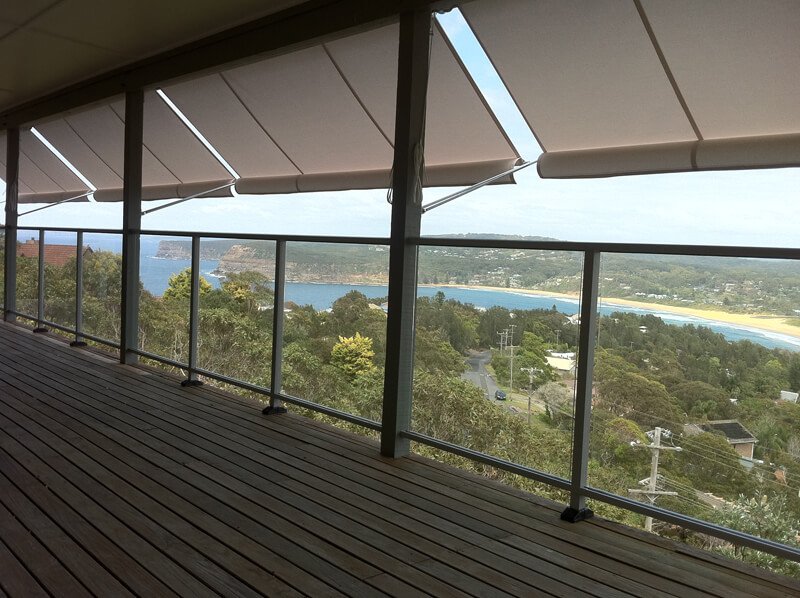 View from a balcony showing trees, a river, and distant land under an overcast sky with partial shade.