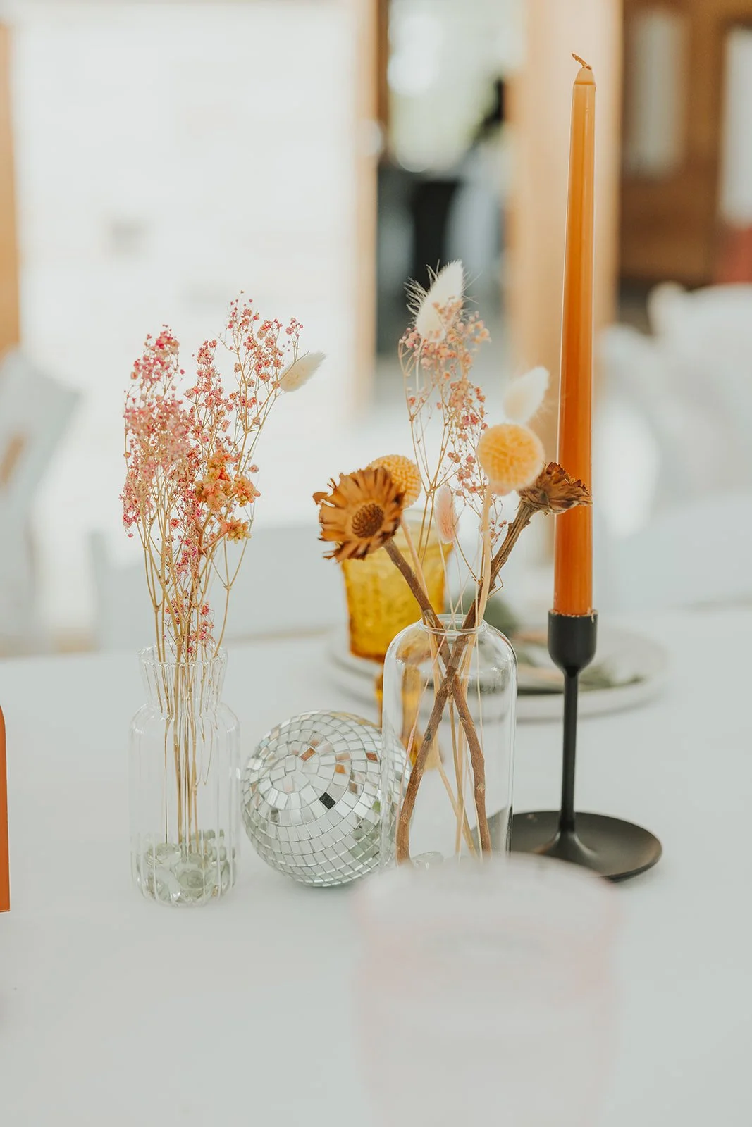 A Design Forward Wedding Reception Tabletop with Wildflower Bud Vases, Black Modern Candlestick Holders, Vintage Amber Goblets, Stoneware Plates By Mountain Arrow Rentals