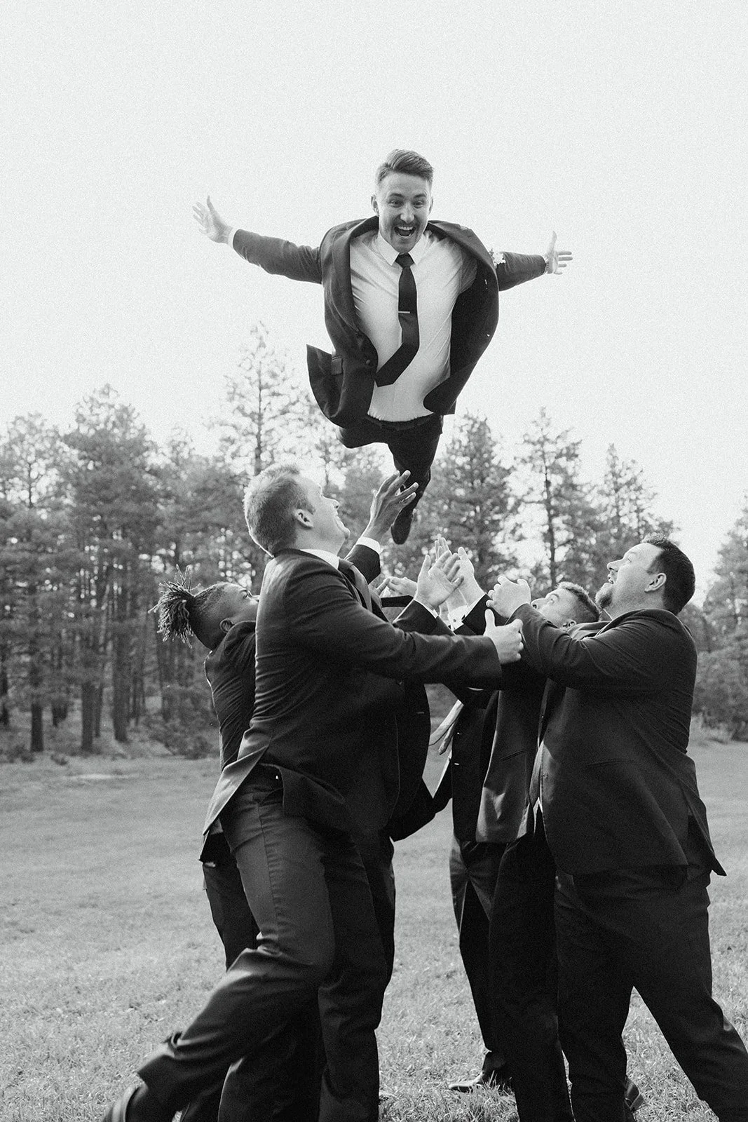 A Black and White Image of A Groom Smiling While Tossed Into The Air By His Groomsmen. Wedding Planned By Mountain Arrow Events and Rentals