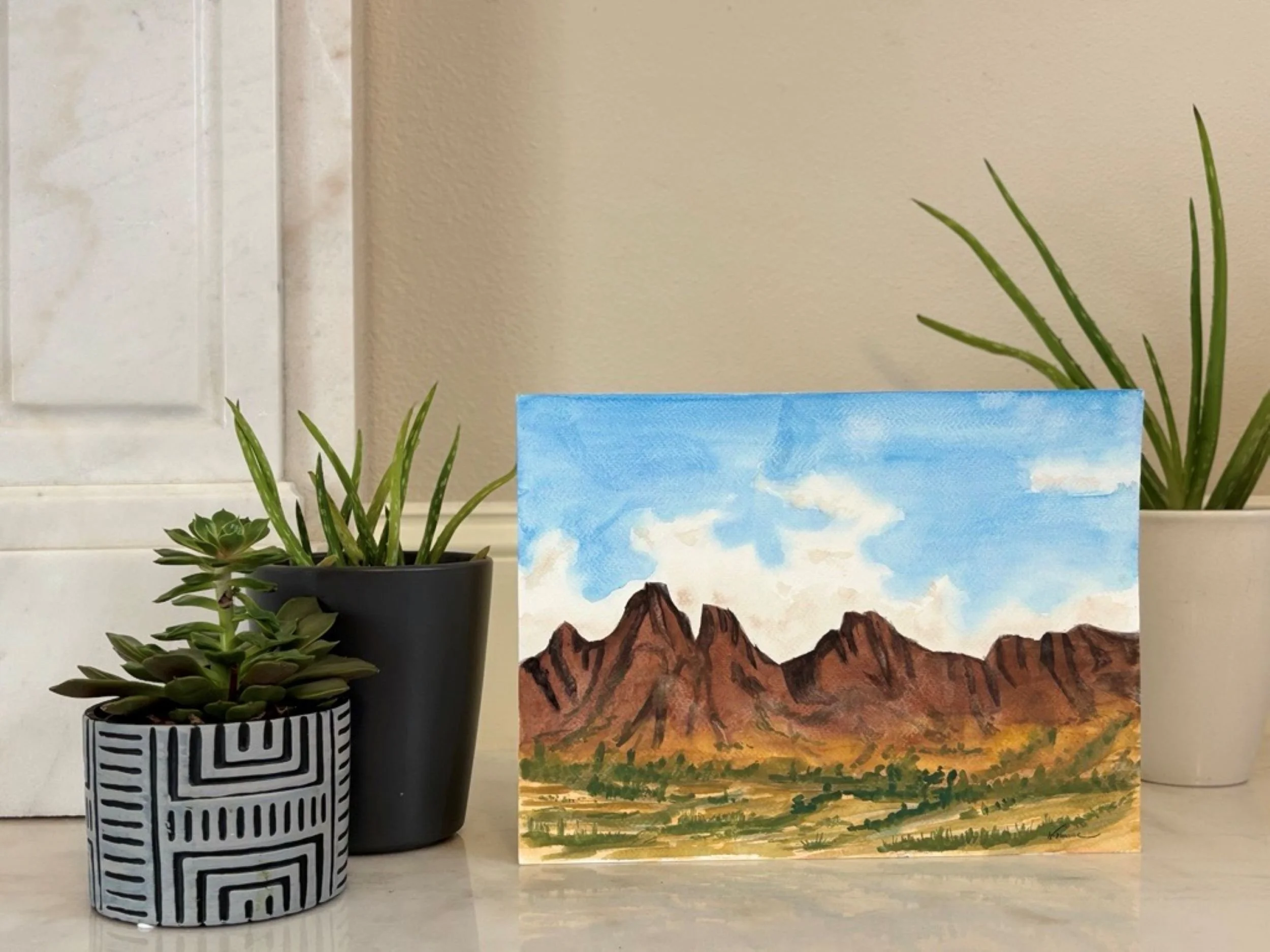 Placed watercolor landscape artwork showing dramatic mountain peaks, deep shadows, and a sunlit valley by Wells