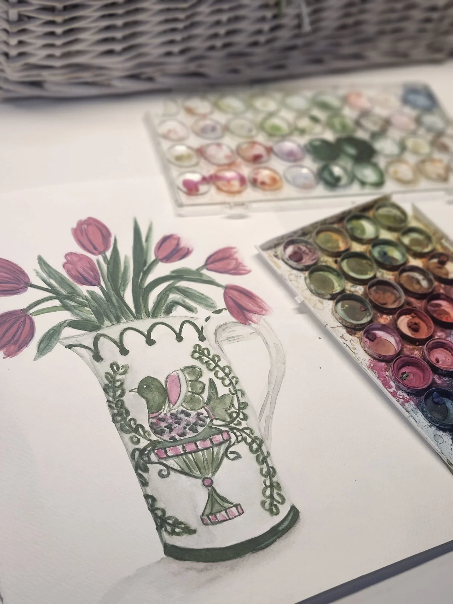 A hand-drawn illustration of a decorative vase with pink tulips in it, using watercolor paints and ink, with watercolor palettes nearby.
