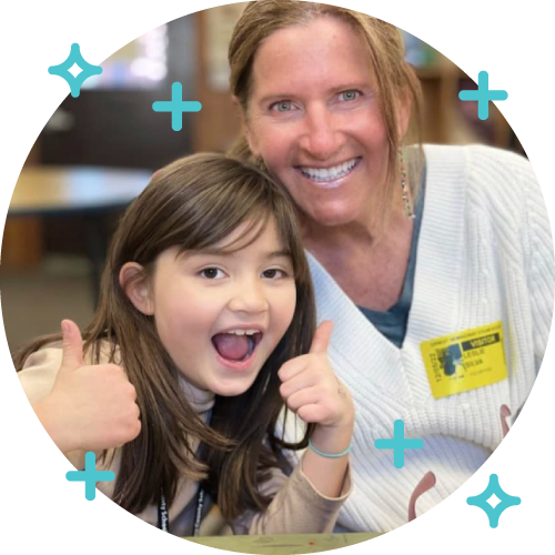 A woman and a young girl smiling and giving thumbs up in an indoor setting.