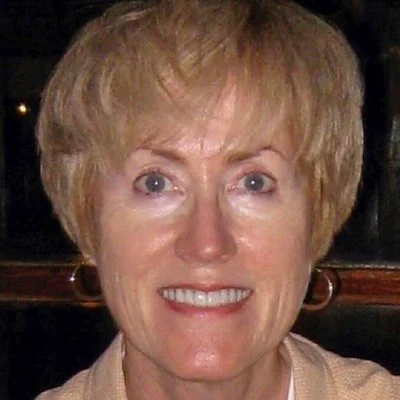 A smiling woman with short, light-colored hair and earrings.