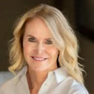 A woman with blonde wavy hair smiling, wearing a white collared shirt.