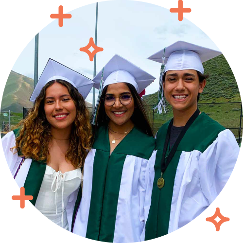 Three graduates in caps and gowns smiling outdoors during graduation ceremony.