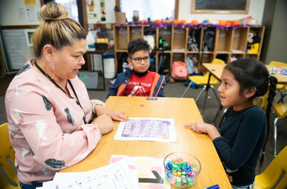 Teacher playing a board game with two children in a classroom.