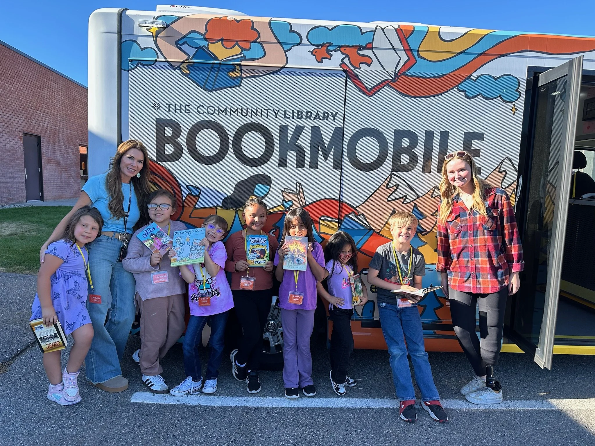 Children and two adults posing in front of a decorated bookmobile with a