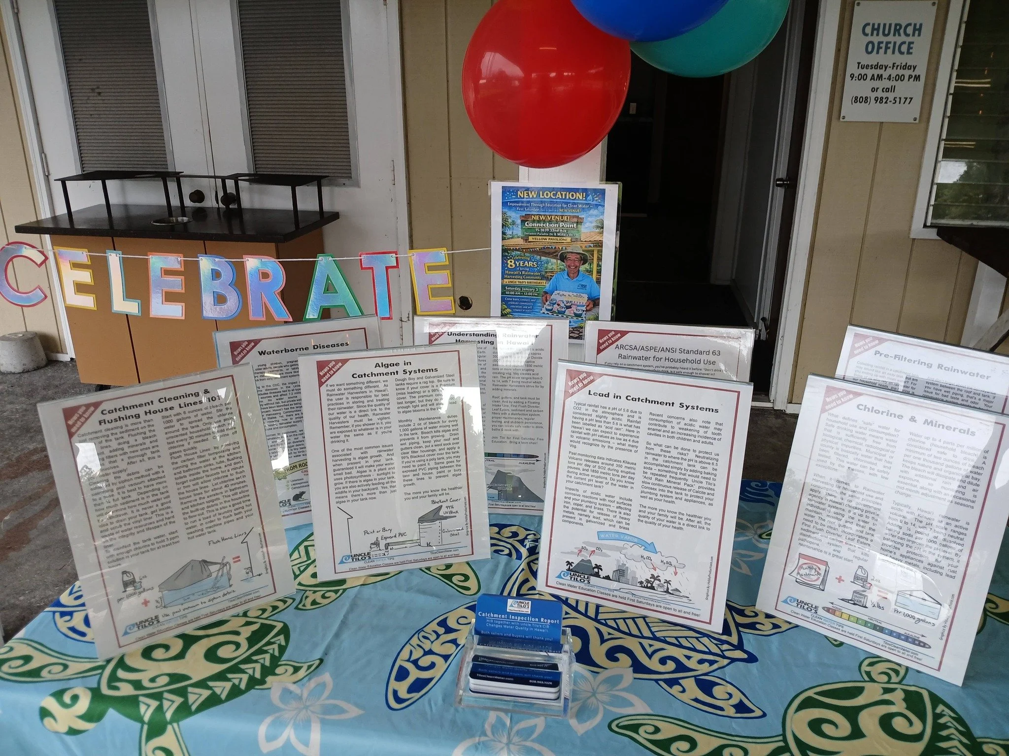 Information display about water-related diseases and water conservation, with balloons and a colorful banner that spells 'CELEBRATE' and a table with informational leaflets.