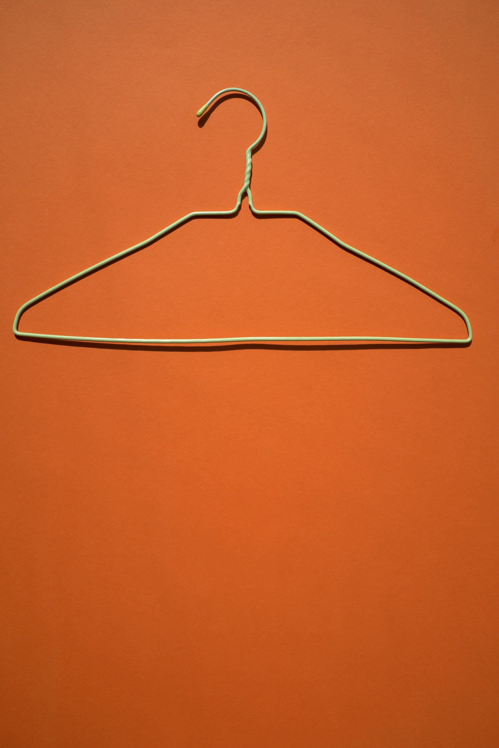 Empty metal hanger hanging on an orange wall.