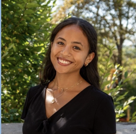 Young woman smiling outdoors with green foliage background.
