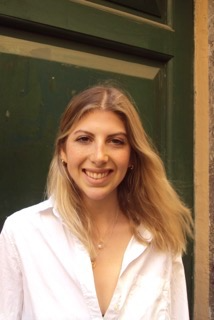 A woman with shoulder-length blonde hair smiling outdoors in front of a green door.