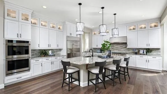 Modern kitchen with white cabinetry, a large island with seating, stainless steel appliances, pendant lighting, and wood flooring.