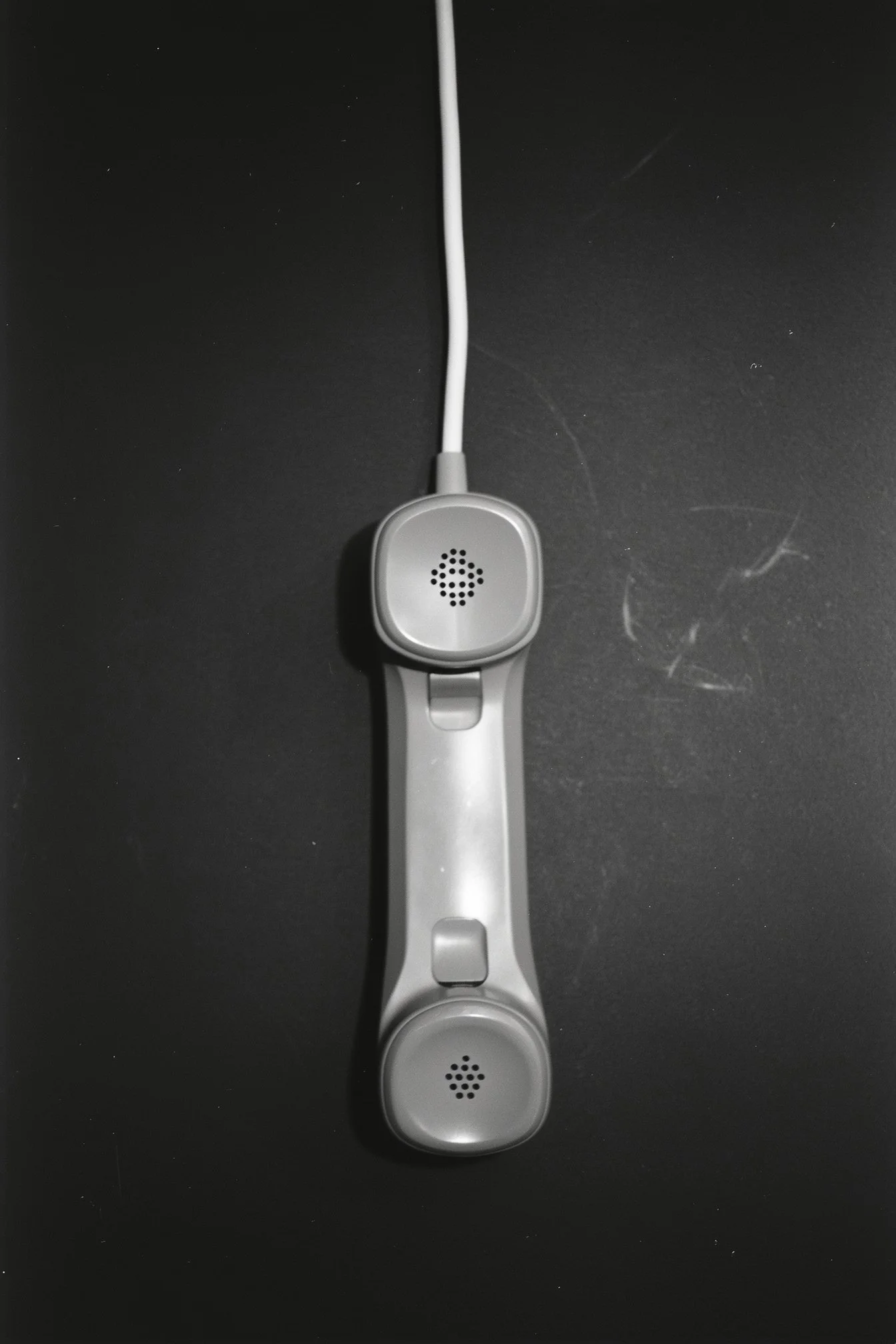 A vintage handheld telephone with a cord, resting on a black surface.