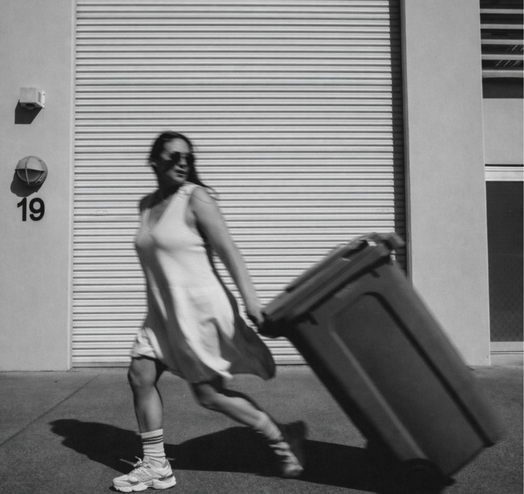 Woman in sunglasses pulling a large suitcase on wheels outside a building with a metal roll-up door.