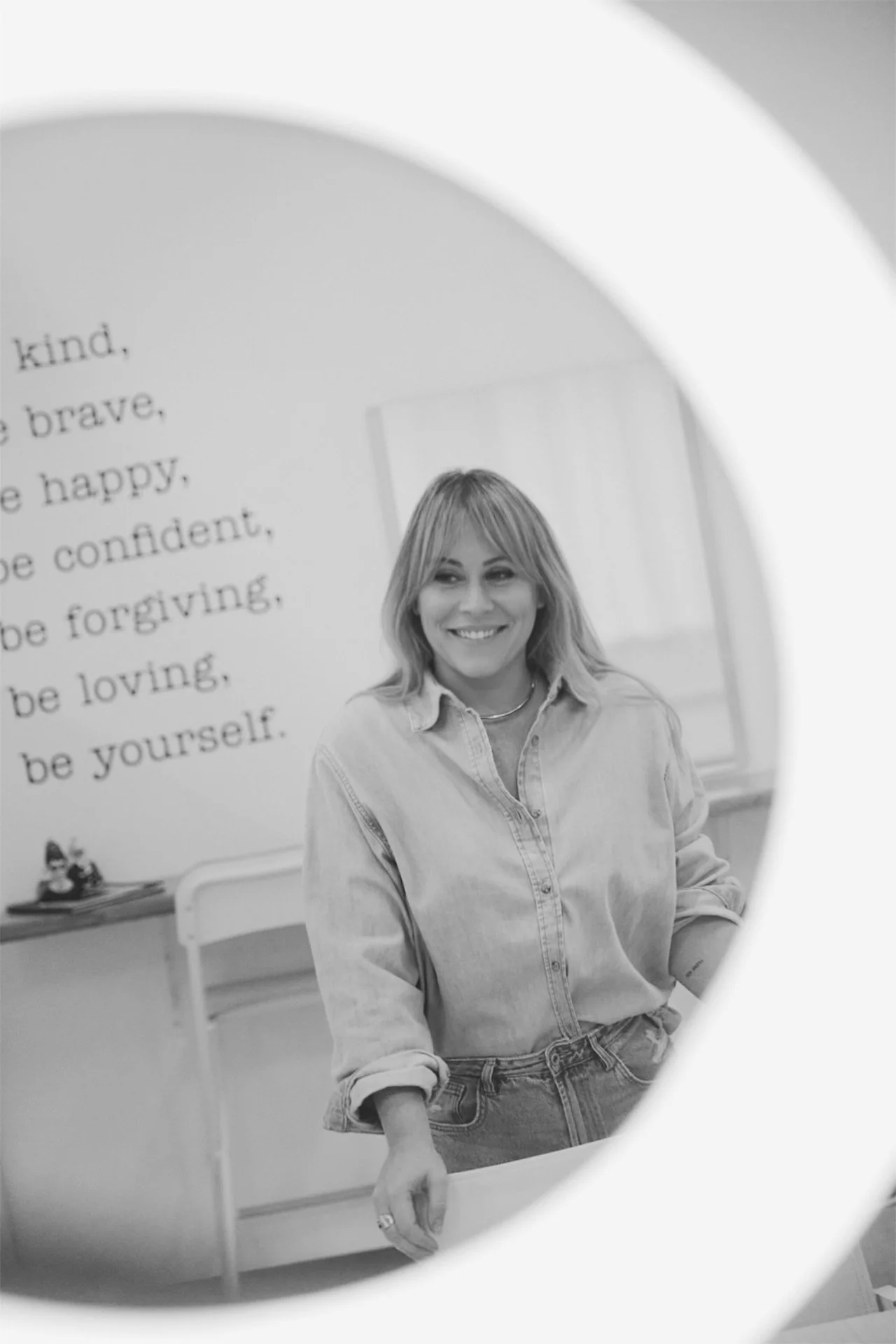 Jacqueline (Jackie) Harris smiling in reflection of a mirror, with a white wall and a motivational quote behind her.