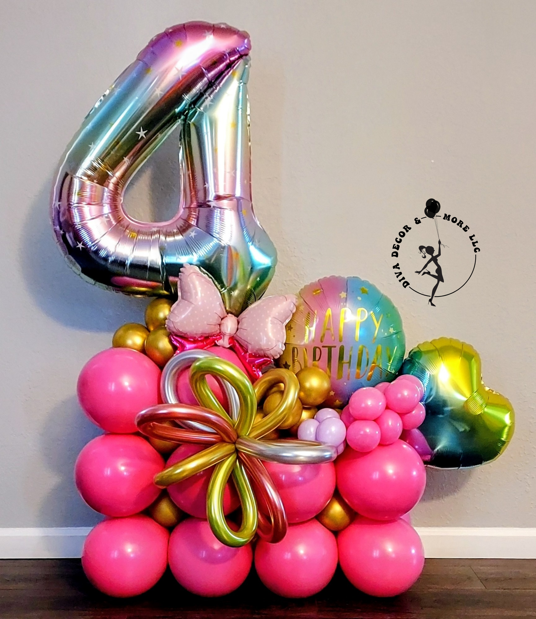 Colorful balloon arrangement including a large number 4 shaped balloon, pink, gold, and multicolored balloons, a butterfly-shaped pink balloon, a 'Happy Birthday' message, and decorative balloon flowers.