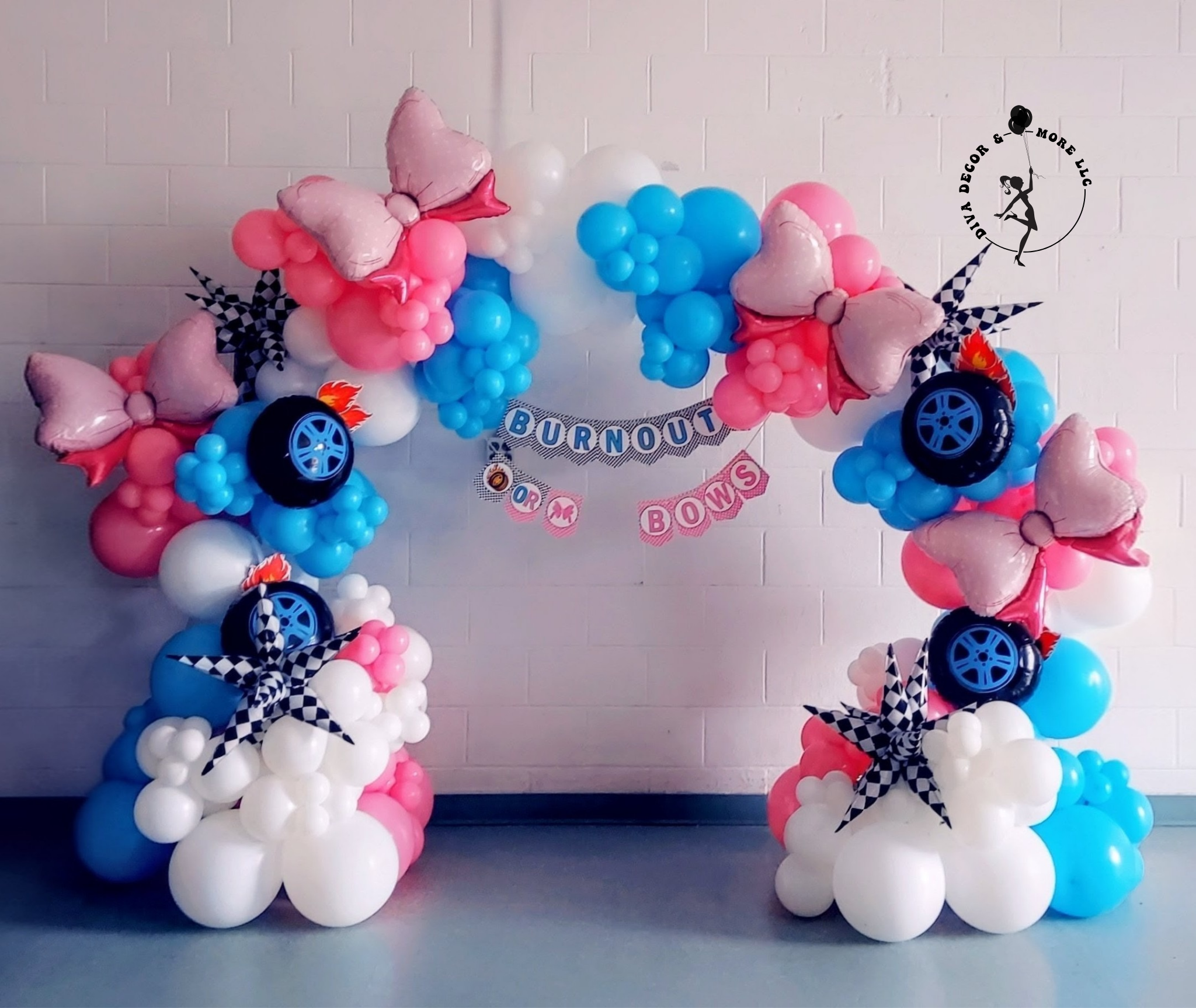 A balloon arch decorated with pink, white, and blue balloons, pink butterfly-shaped balloons, black and white checkered ribbon bows, toy car balloon decorations, and a banner in the center that reads 'BURNOUT OR BOWS' against a white brick wall background.