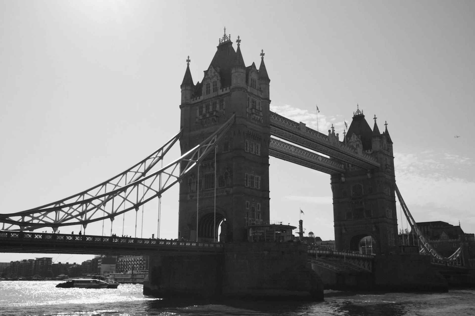 Black and white photo of Tower Bridge in London, with a boat on the river below.