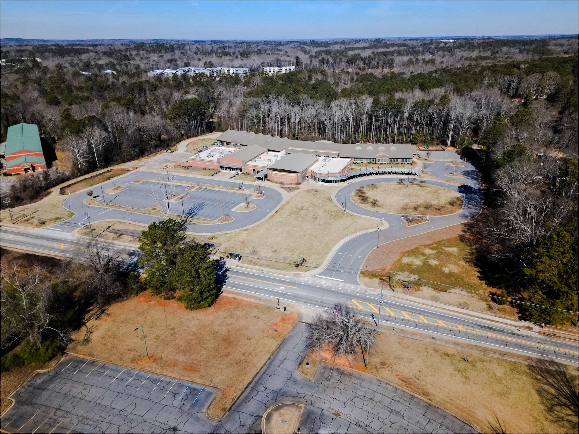 Aerial view of a large, mostly empty parking lot and a school building surrounded by trees.