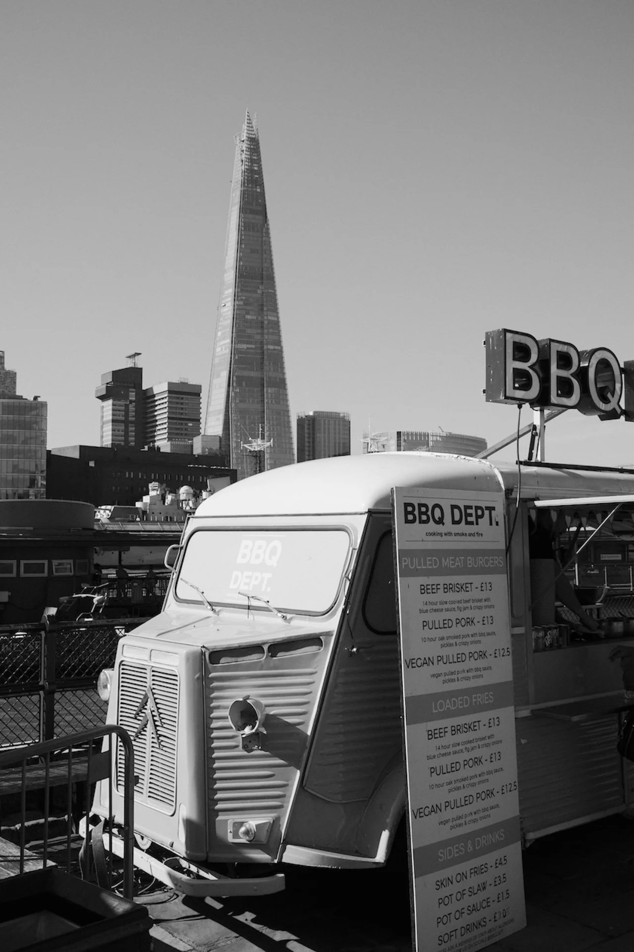 A food truck labeled 'BBQ DEPT.' with a menu, parked outdoors with city buildings and the Shard skyscraper in the background.