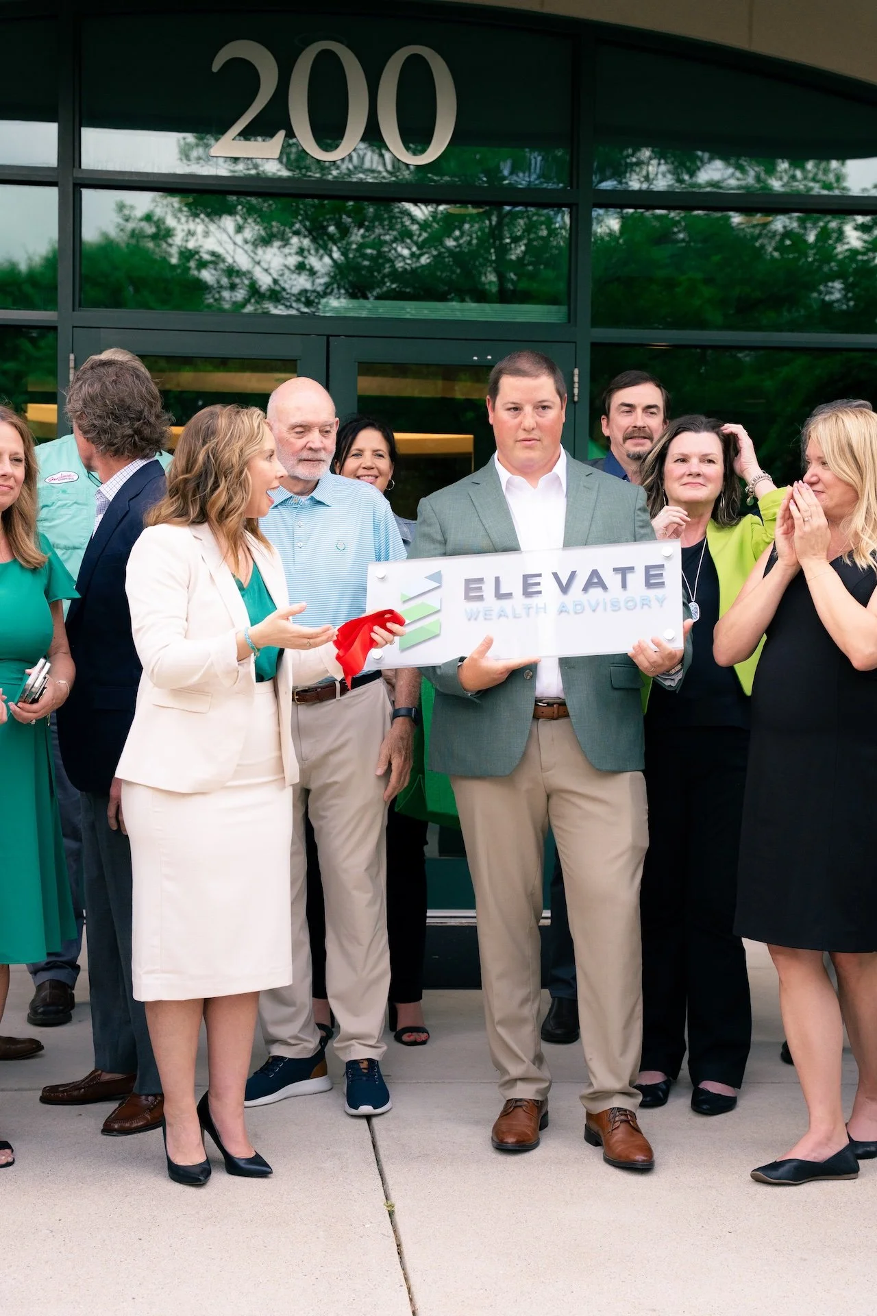 Group of people standing outside a building, holding a sign that reads 'Elevate Wealth Advisory', with the number 200 above the entrance.