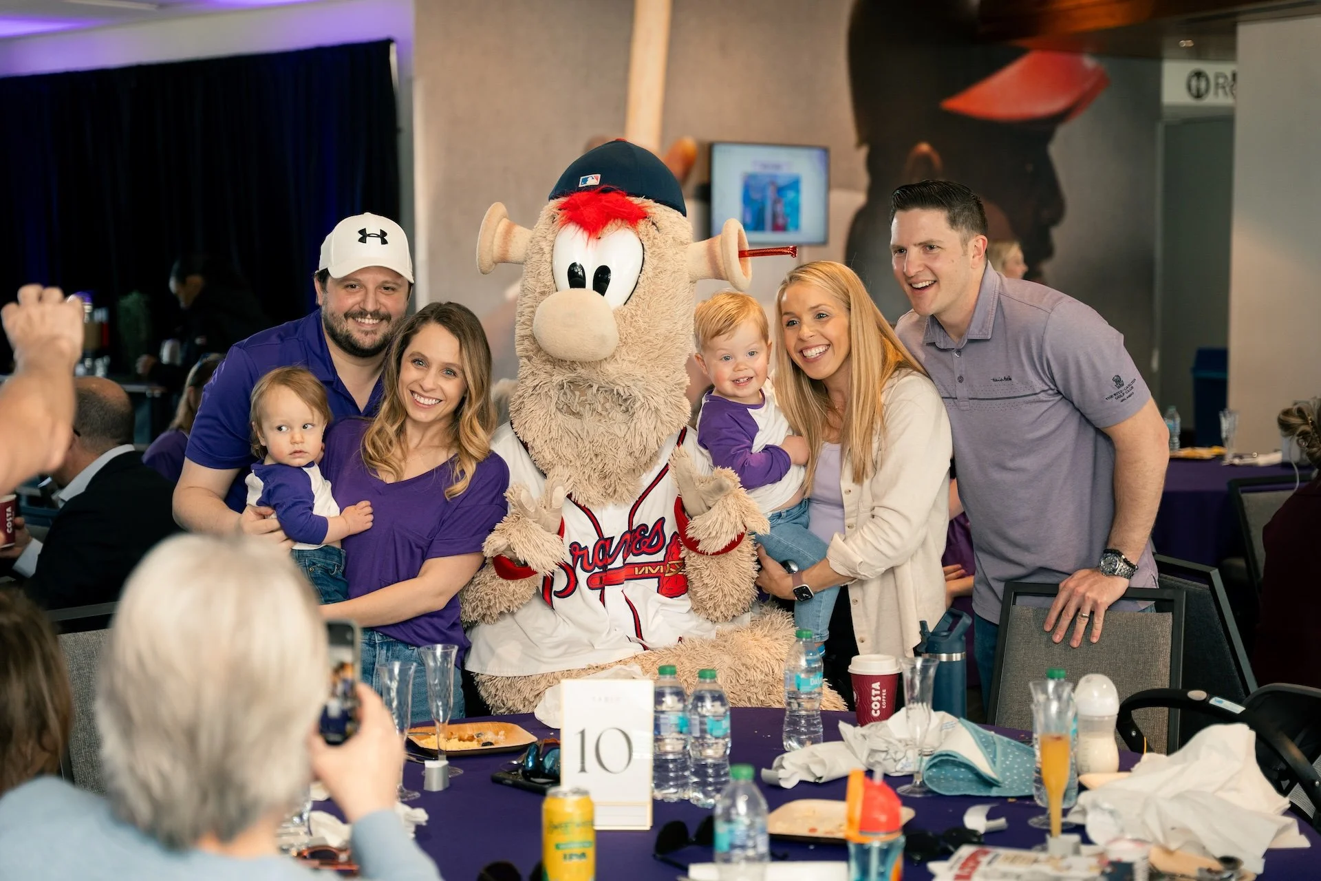 Group of people posing with a baseball mascot in a banquet hall.