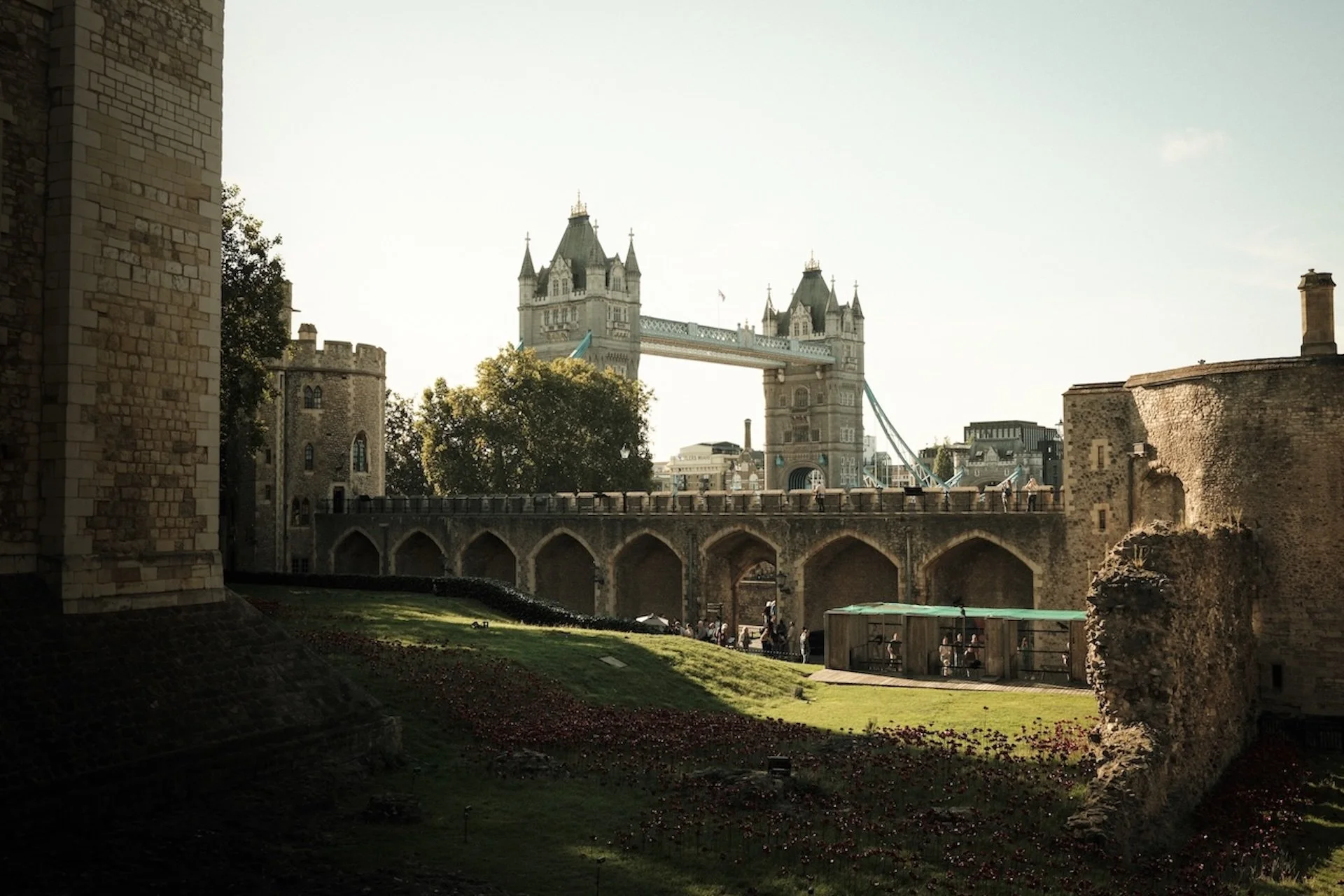 View of Tower Bridge in London with a bridge connecting two towers and a castle-like structure in the foreground, under a bright sky.