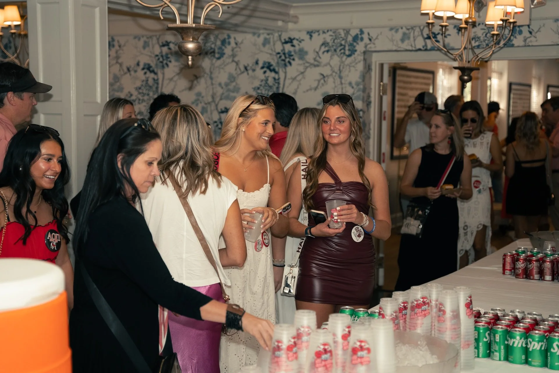 Group of women at a social gathering with drinks and snacks, chatting and smiling.