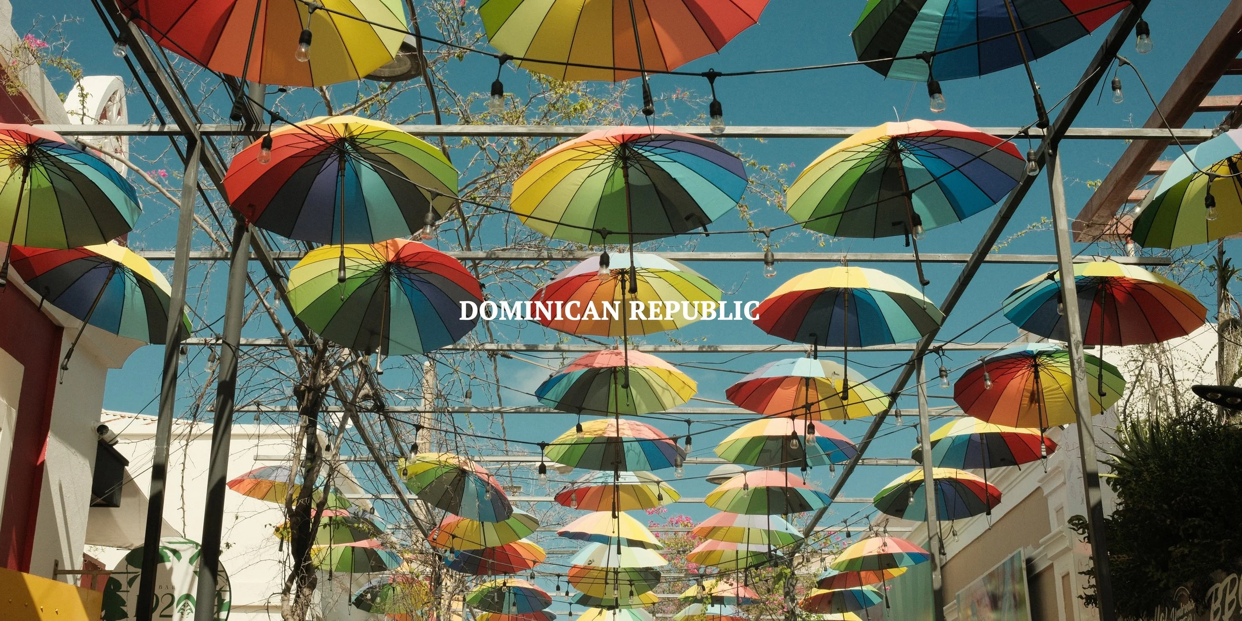 Colorful umbrellas hanging above a street in the Dominican Republic with blue sky in the background.