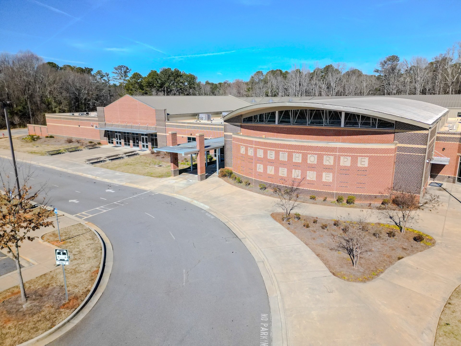 Aerial view of Ogletree Elementary School building with a brick exterior, surrounded by parking lot and trees, under a bright blue sky.