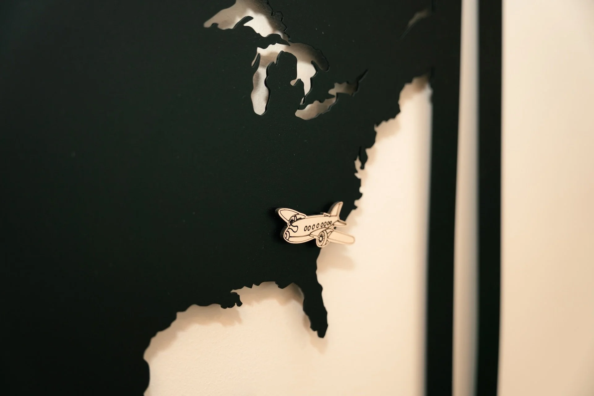 Black wall decor of North America with a small airplane magnet near the southern coast of the United States.