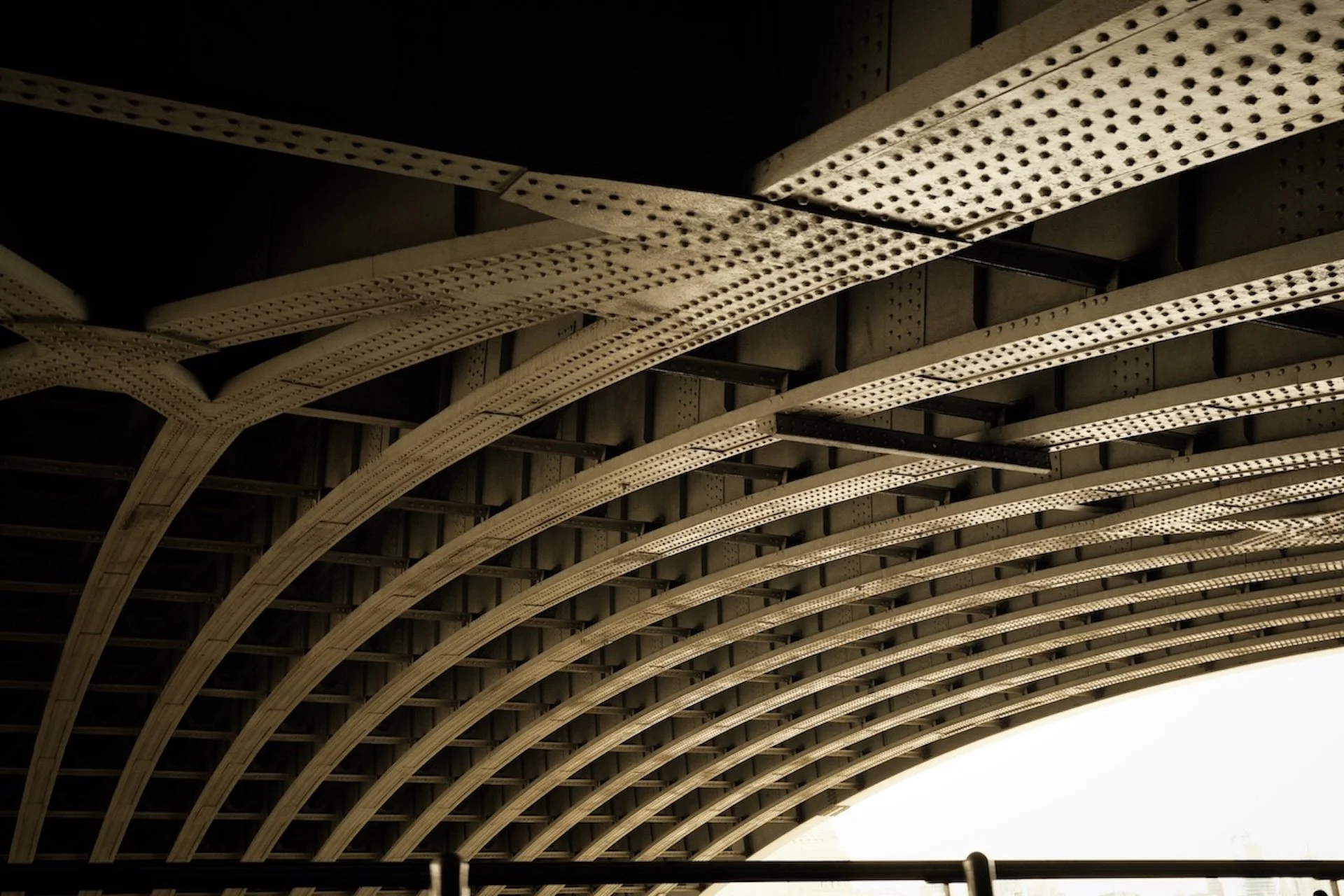 Close-up view of an arched steel bridge with riveted beams and girders, showing structural details and curves.