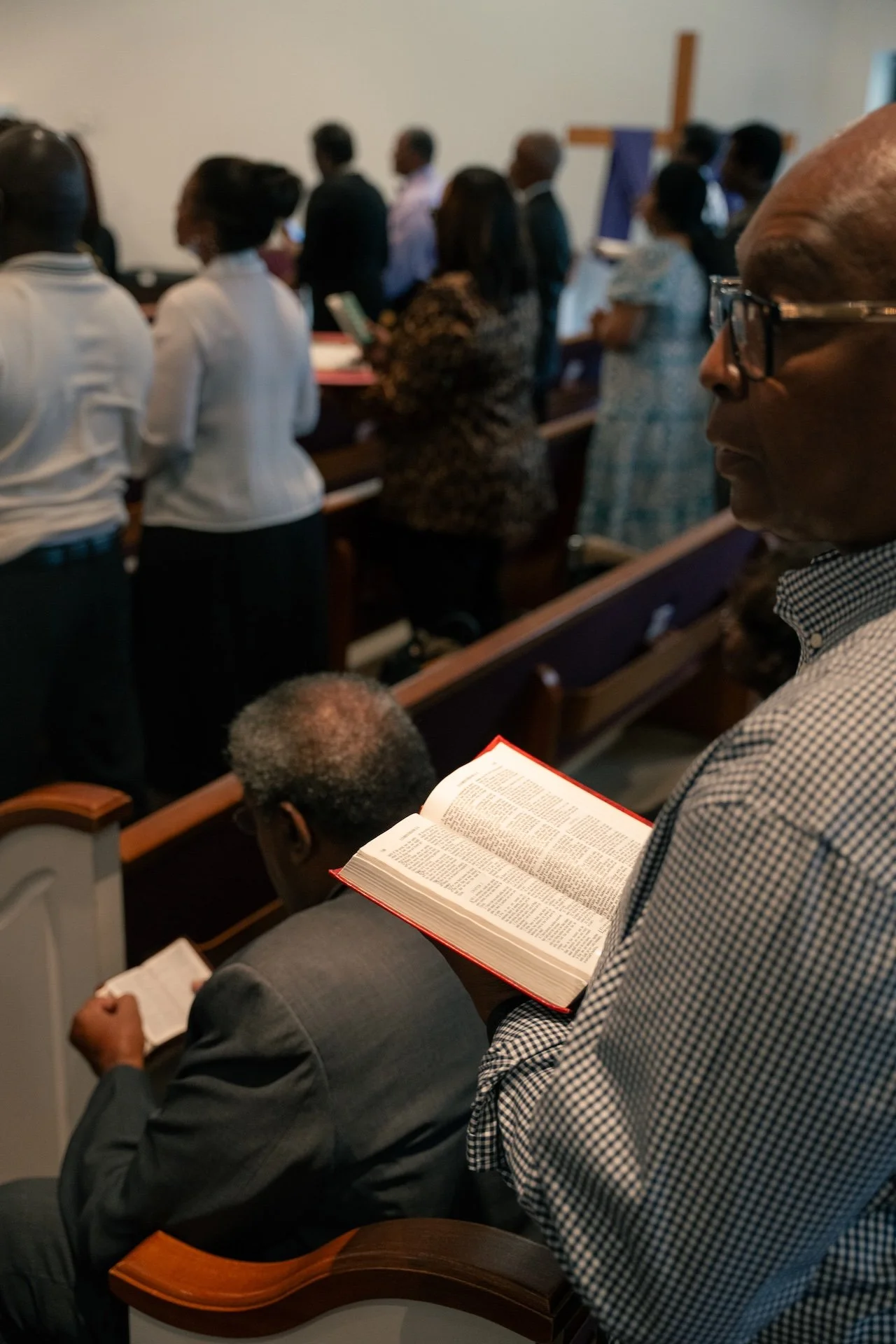 People attending a church service, standing and reading their Bibles in a chapel.