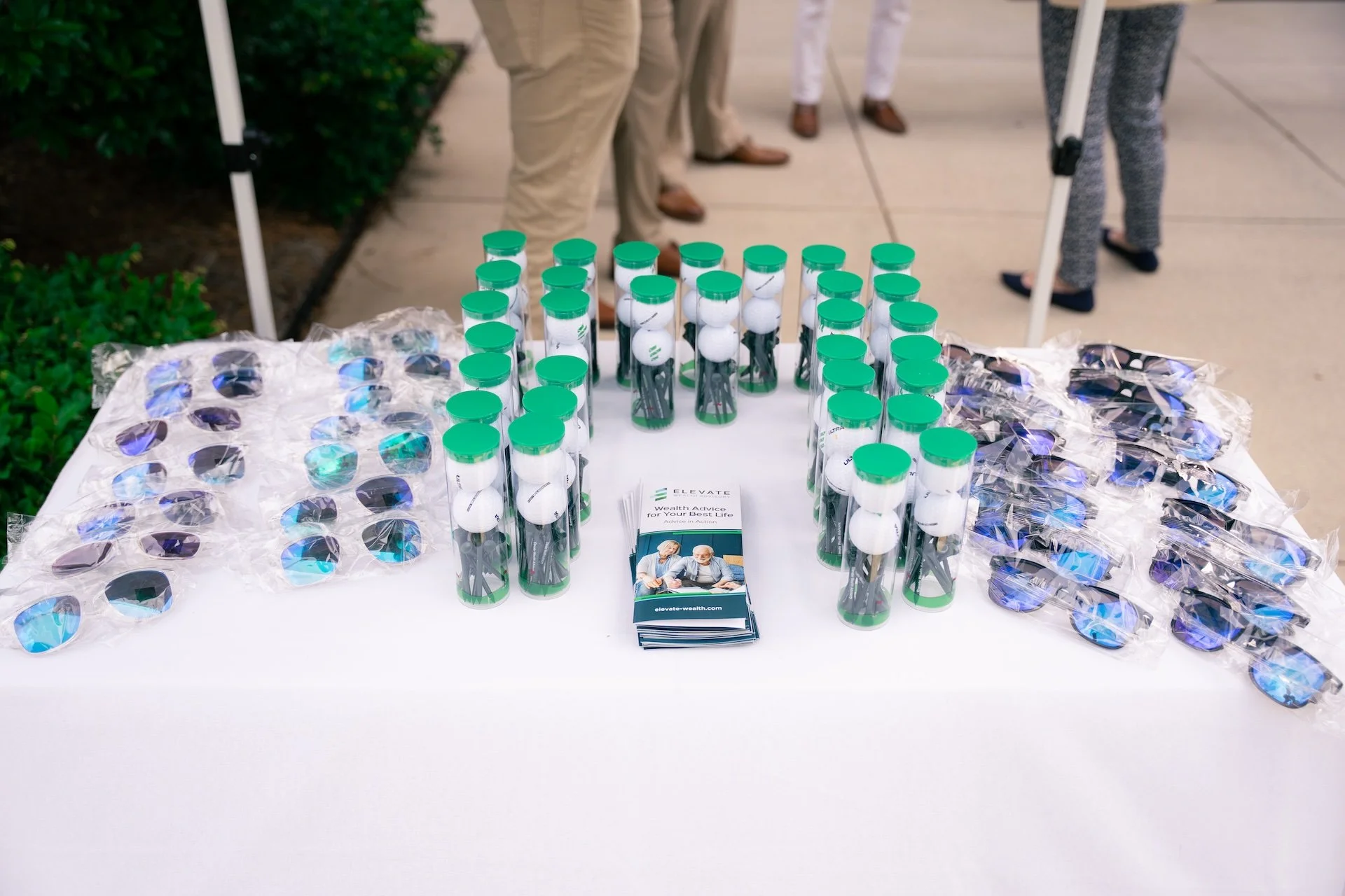 Table with branded golf balls and sunglasses at an outdoor event.