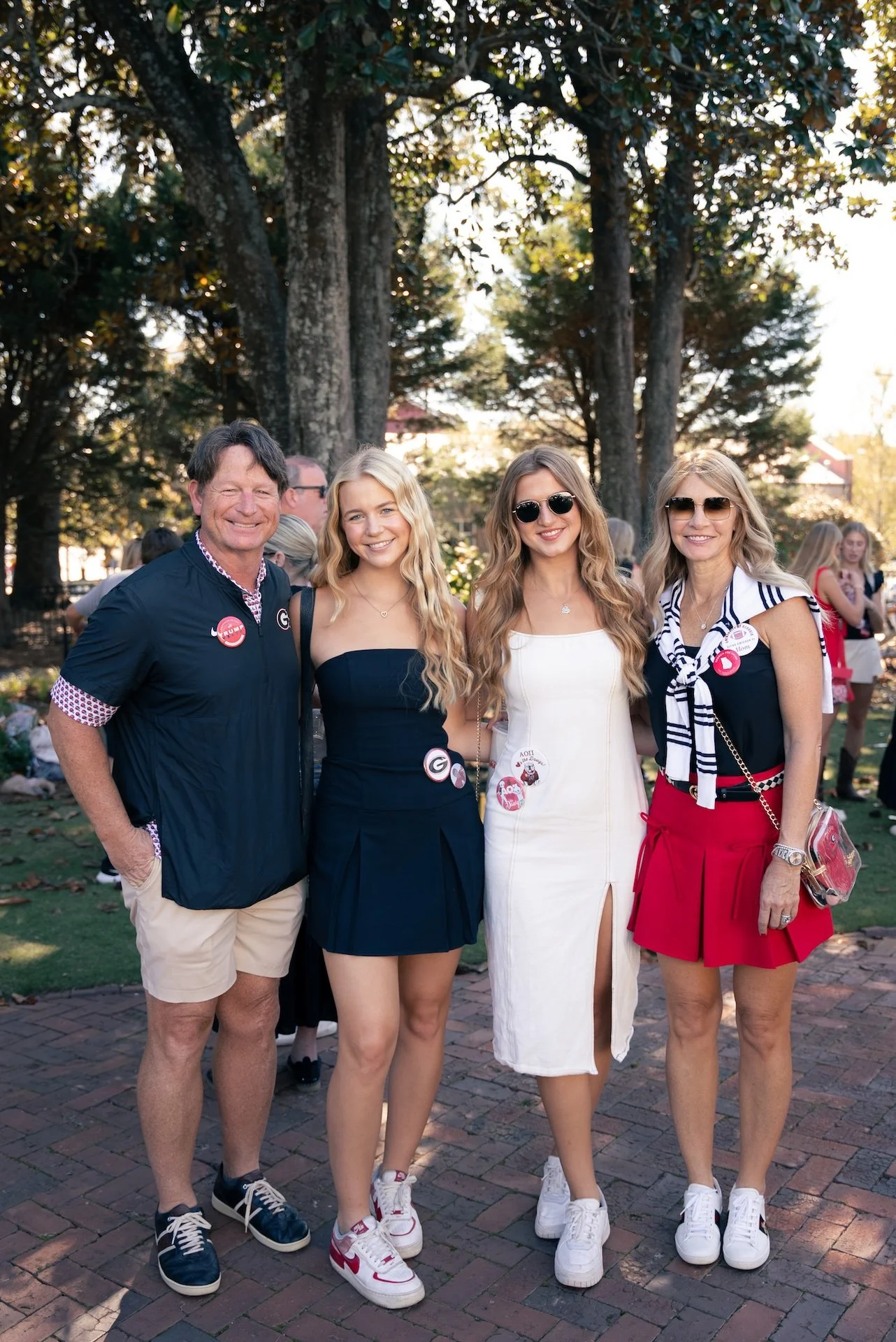 Group of four people standing outdoors during the daytime, smiling, with trees and other people in the background.