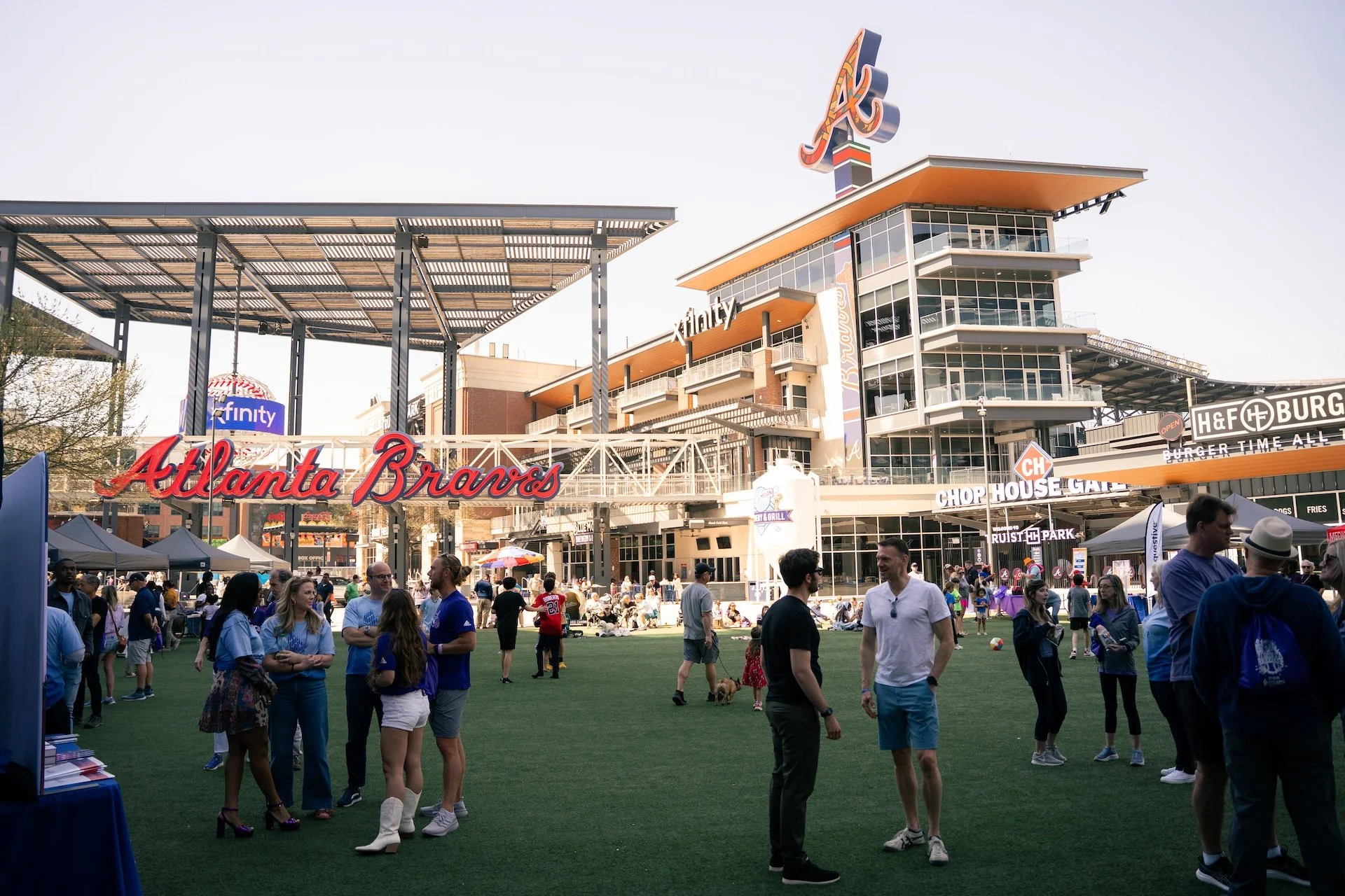 People gathering outside at a baseball stadium with signs for Atlanta Braves and a restaurant called H&F Burger.