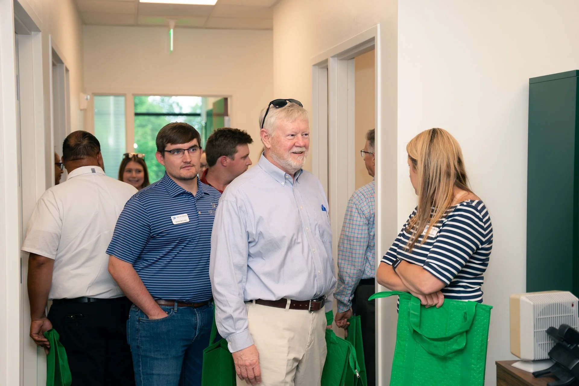 Group of people in a hallway waiting in line, engaging in conversation with a woman behind a desk.