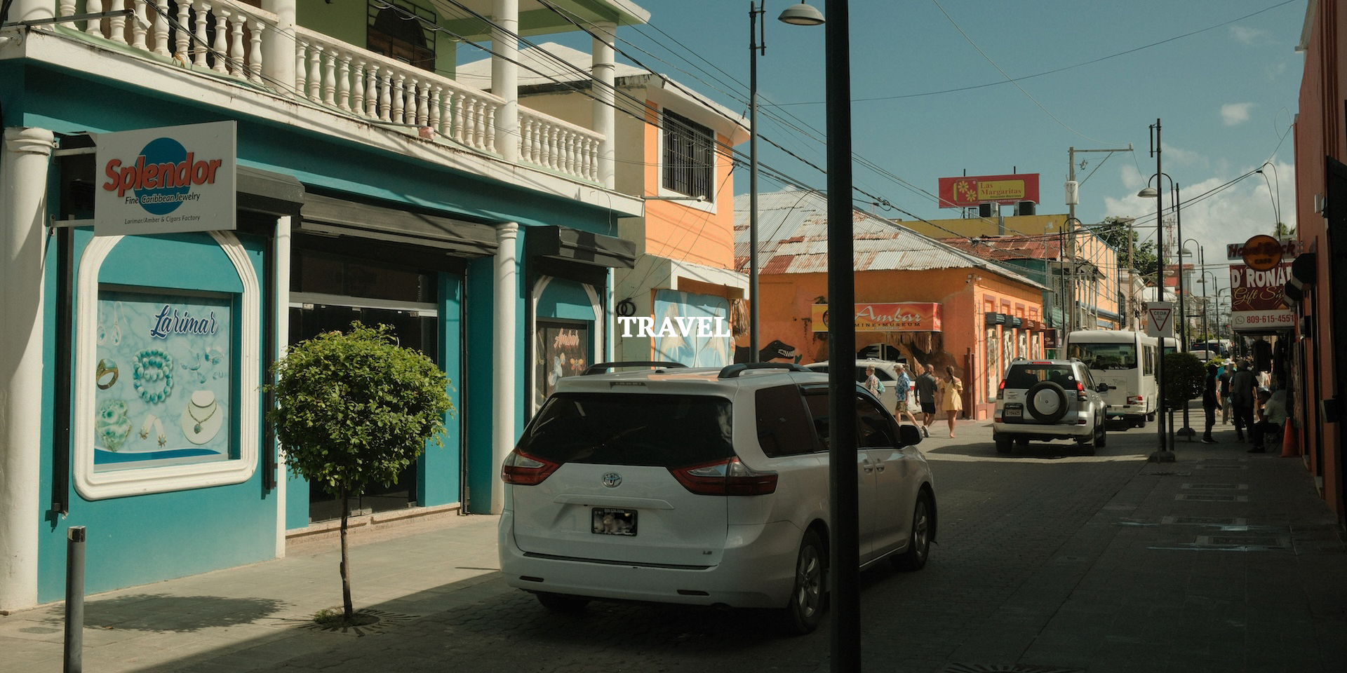 Street scene with cars parked along sidewalk, storefronts, and pedestrians walking, under a partly cloudy sky.