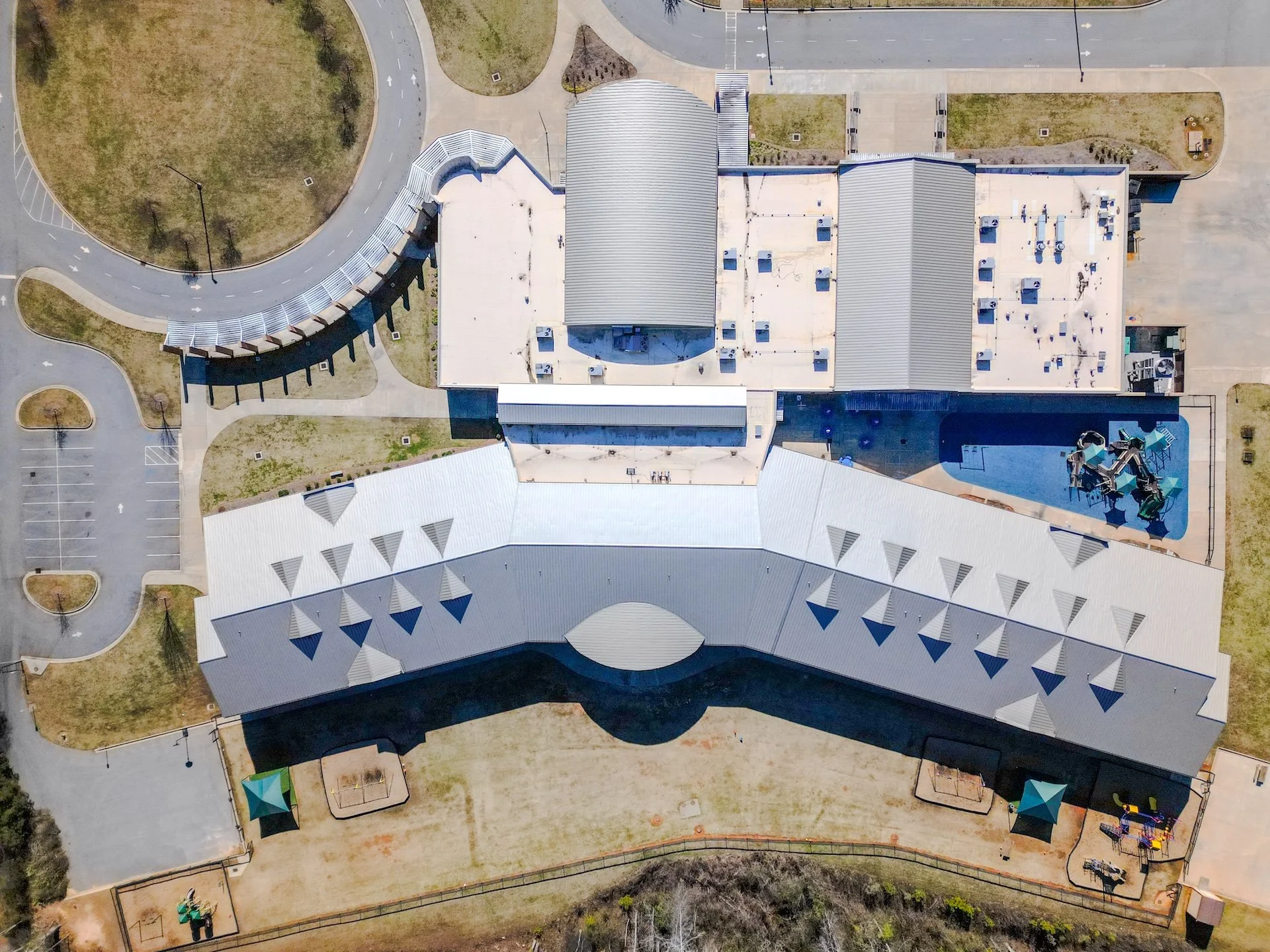 An aerial view of a school building with a playground, parking lot, and surrounding green areas.