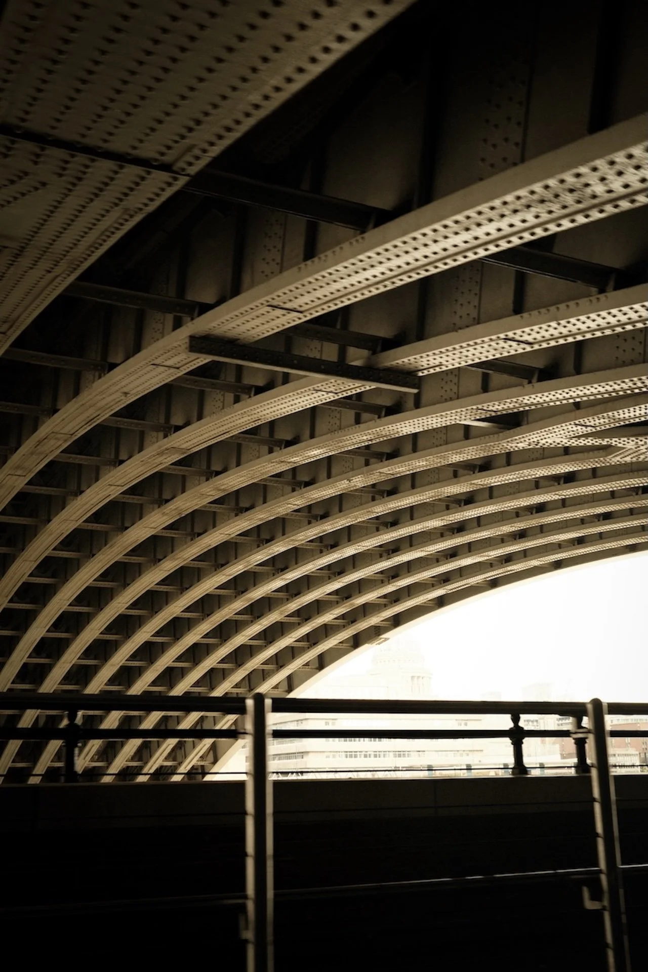 View of an arched bridge or building roof with a detailed metal structure, with a bright cityscape visible through the opening.