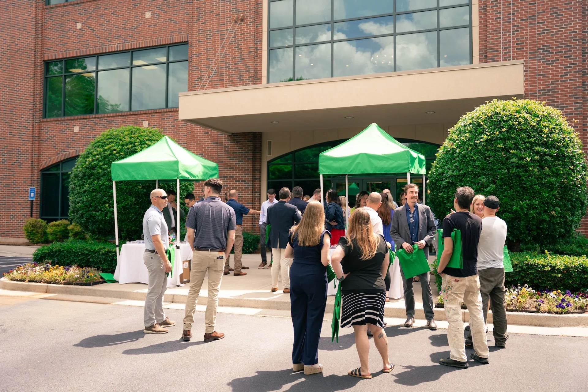 People gathered outside a building with green tents and decorations, possibly attending an event or celebration.
