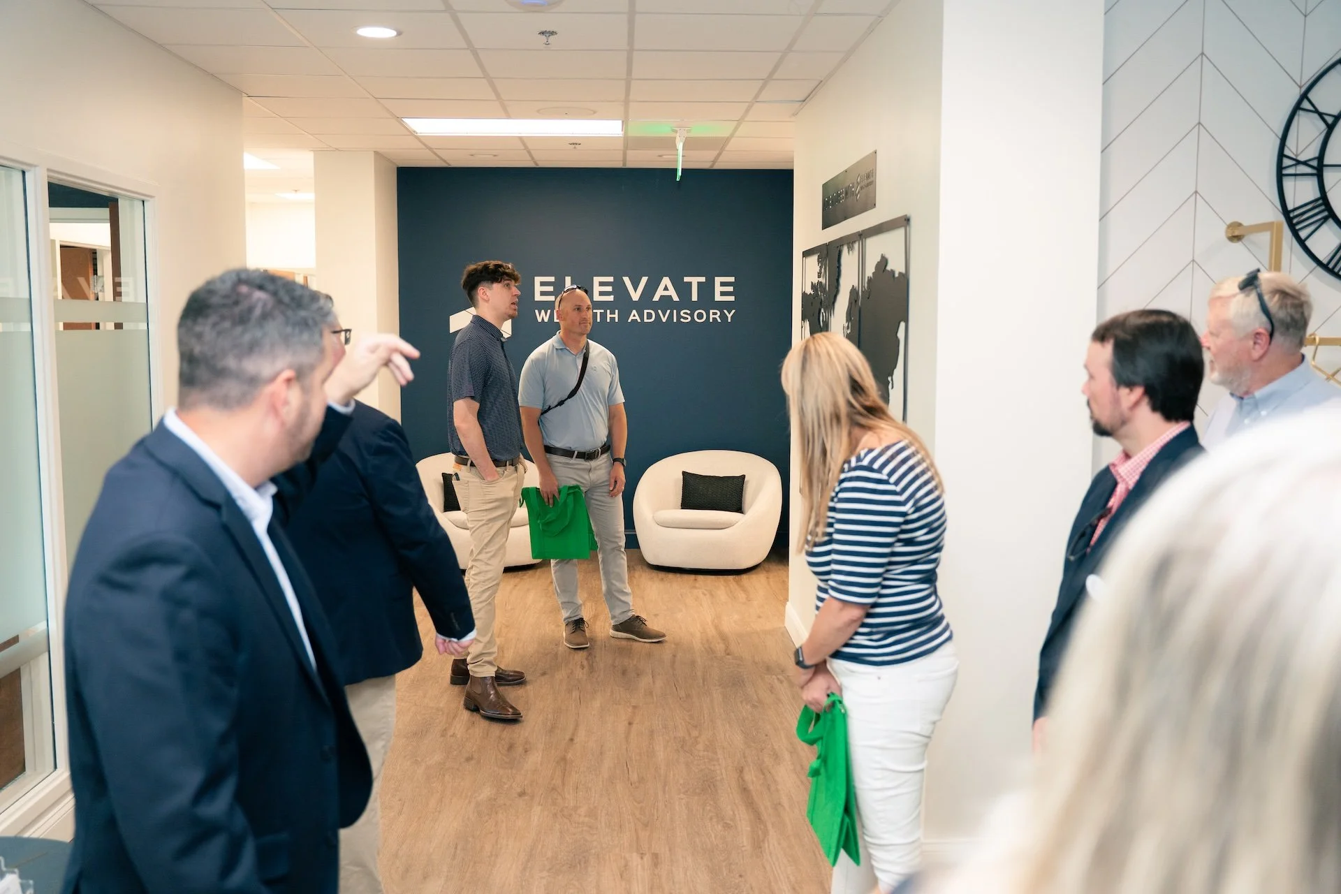 Group of people standing and talking in an office lobby with a blue wall that says 'ELEVATE WITH ADVISORY'.
