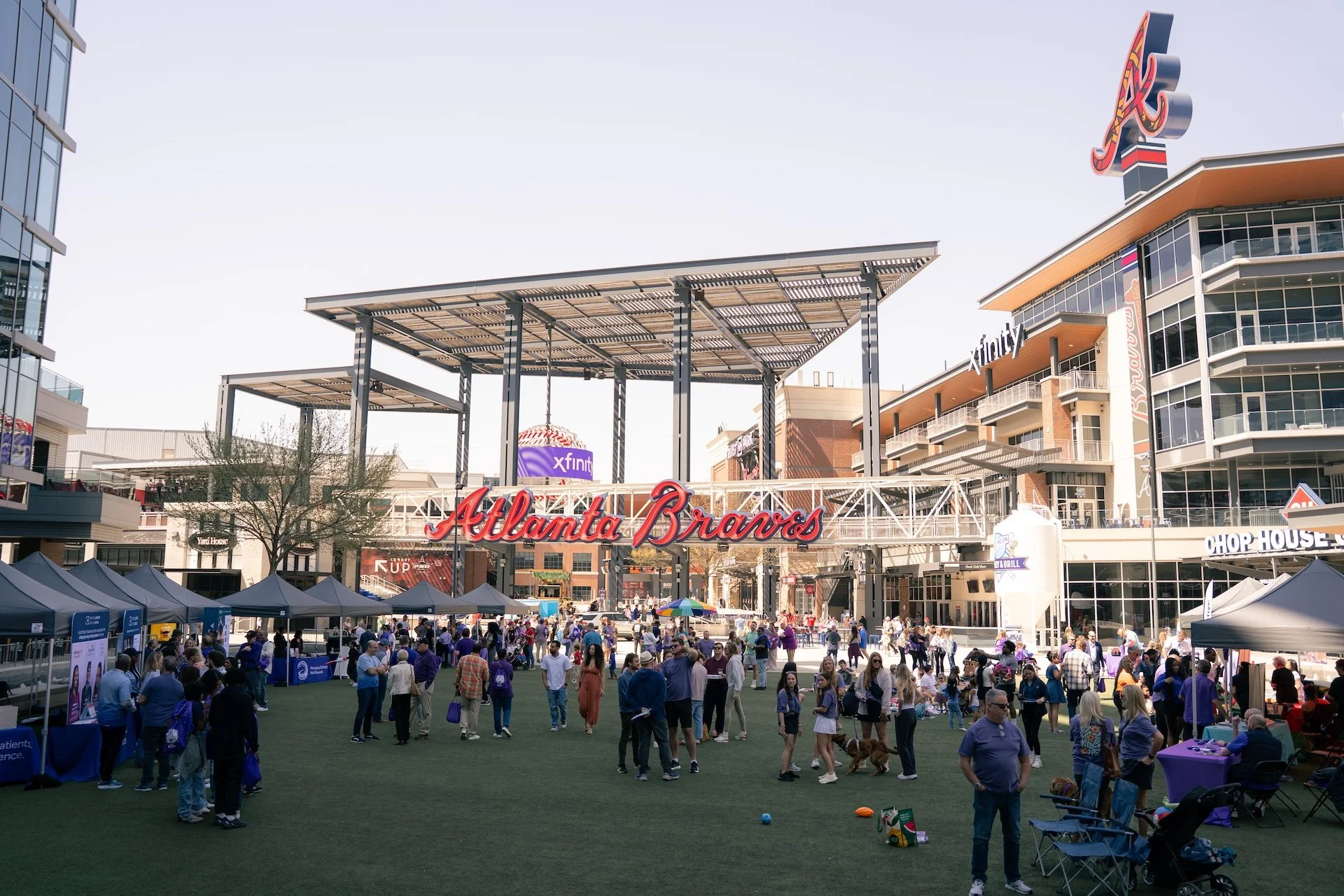 Crowd of people gathered outside Atlanta Braves stadium, with tents, vendors, and people walking dogs on a sunny day.