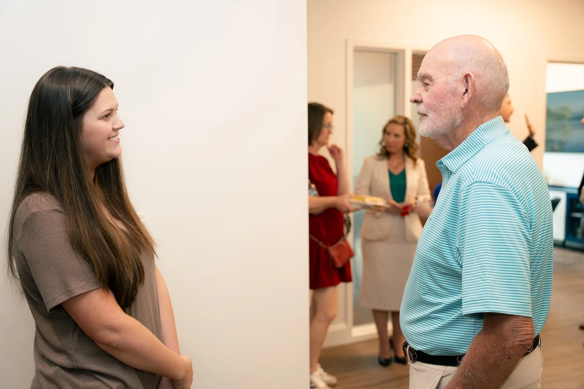 A young woman and an older man smiling at each other during a social gathering.