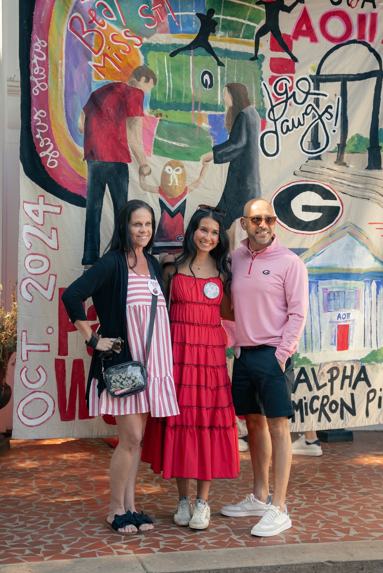 Three people standing in front of a colorful painted wall celebrating a sorority event, with decorations and artwork including the Greek letter Alpha Sigma Tau and the number 124.