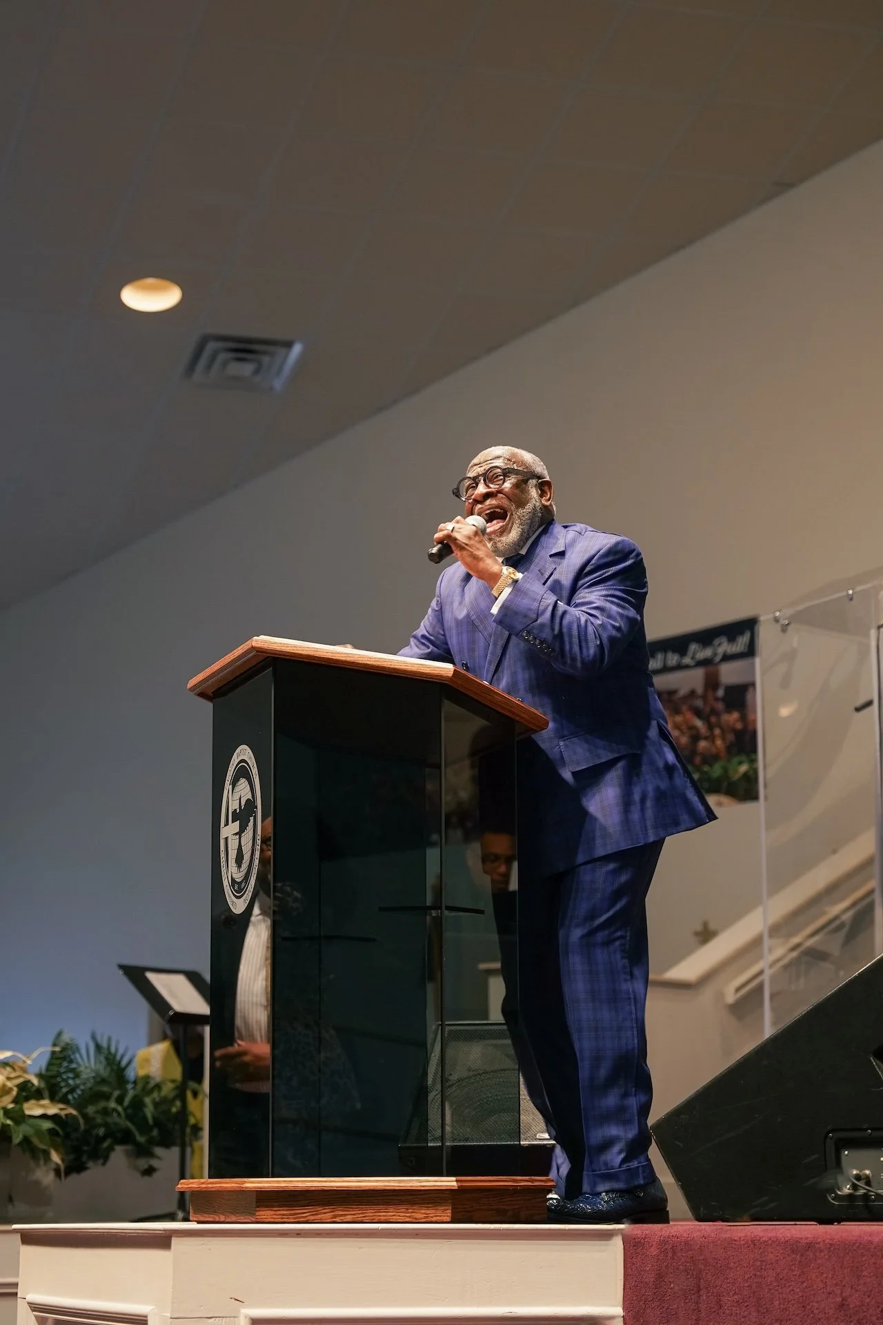 An elderly man in a blue suit passionately speaking or singing at a podium during an event.