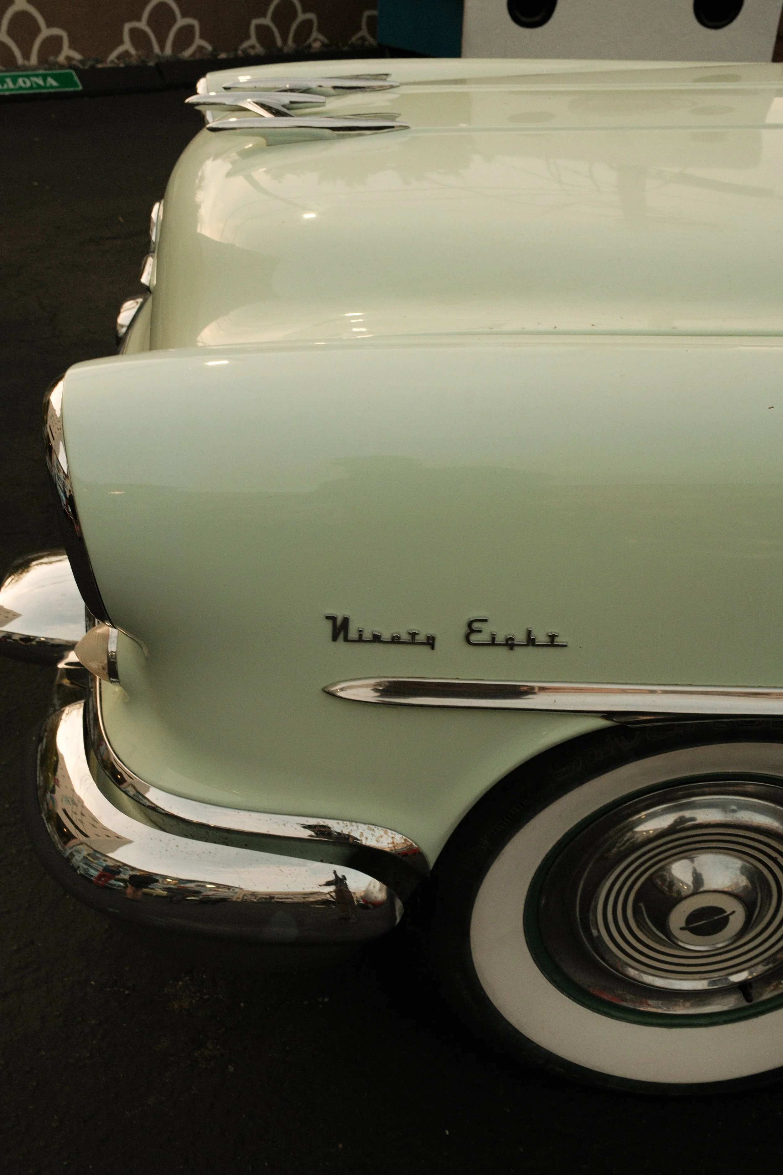 Close-up of a vintage light green Cadillac car, showing part of the front and side, with the emblem 'Ninety Eight' on the side and whitewall tires.