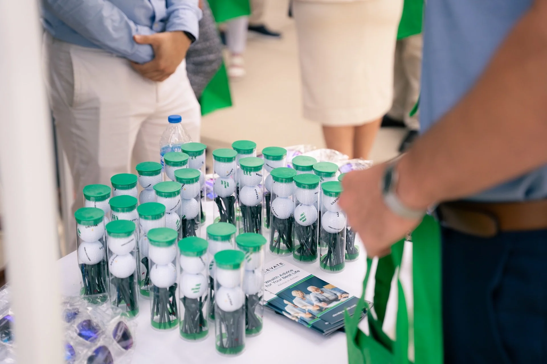 Table with multiple containers of golf balls, each holder has a green lid, and there are brochures and a water bottle on the table.