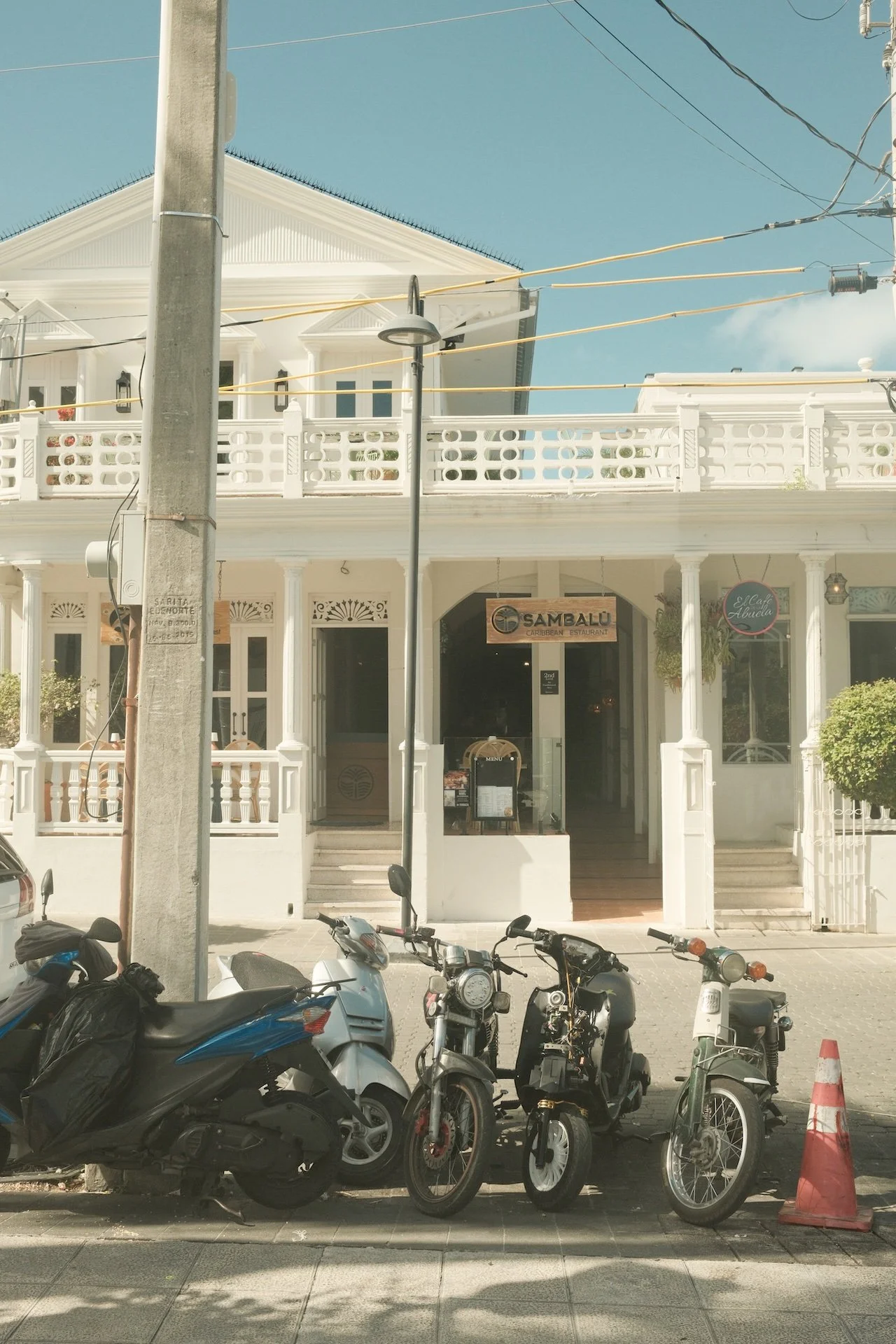 Street view of a white Caribbean restaurant with motorcycles parked in front and a traffic cone on the sidewalk.